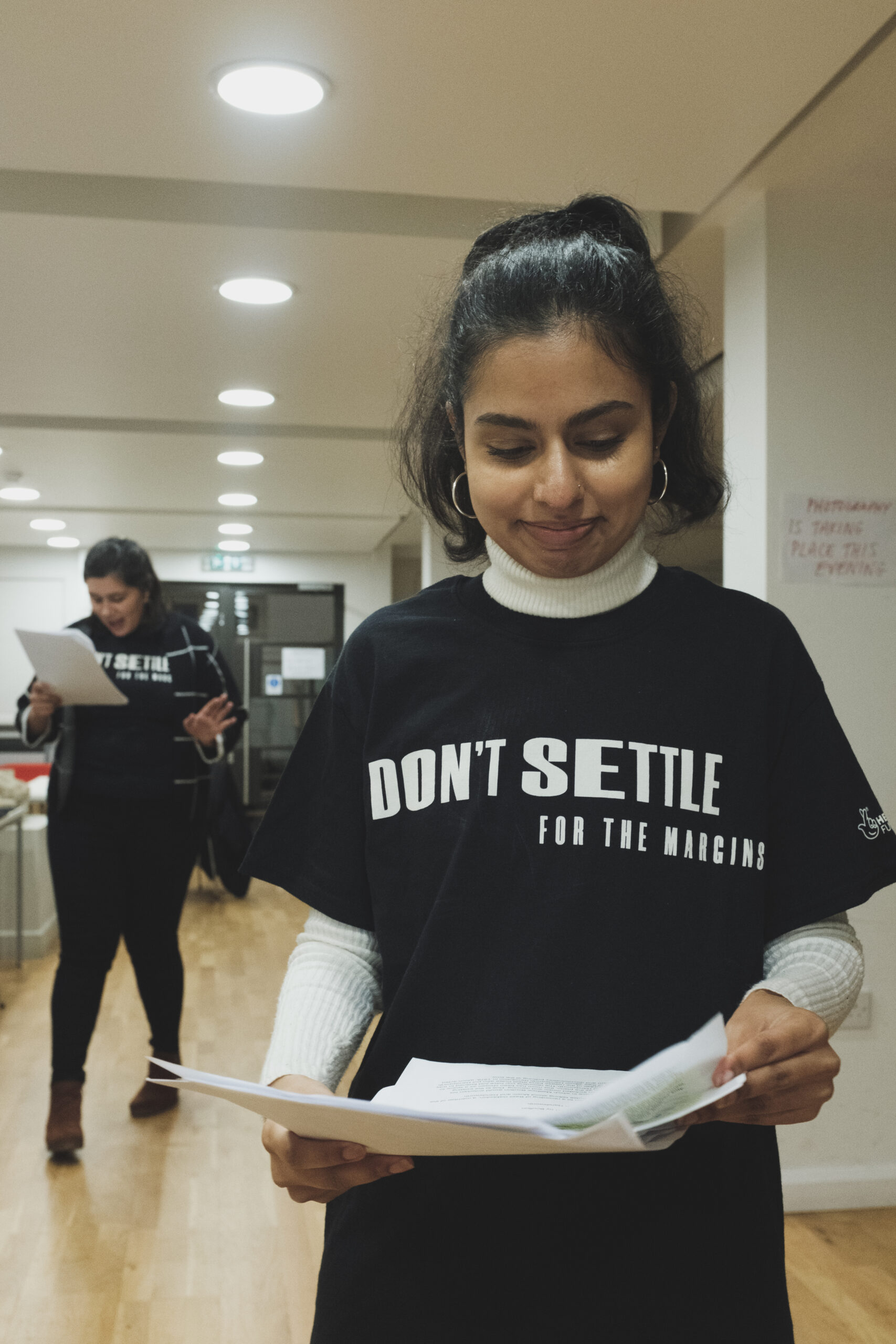 A young woman of colour, wearing a black tshirt with the slogan "Don't Settle for the Margins" reads her notes as she prepares for a Lunar Campfire.